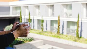 Una persona sosteniendo una taza, con vistas a un edificio moderno con balcón de cristal.