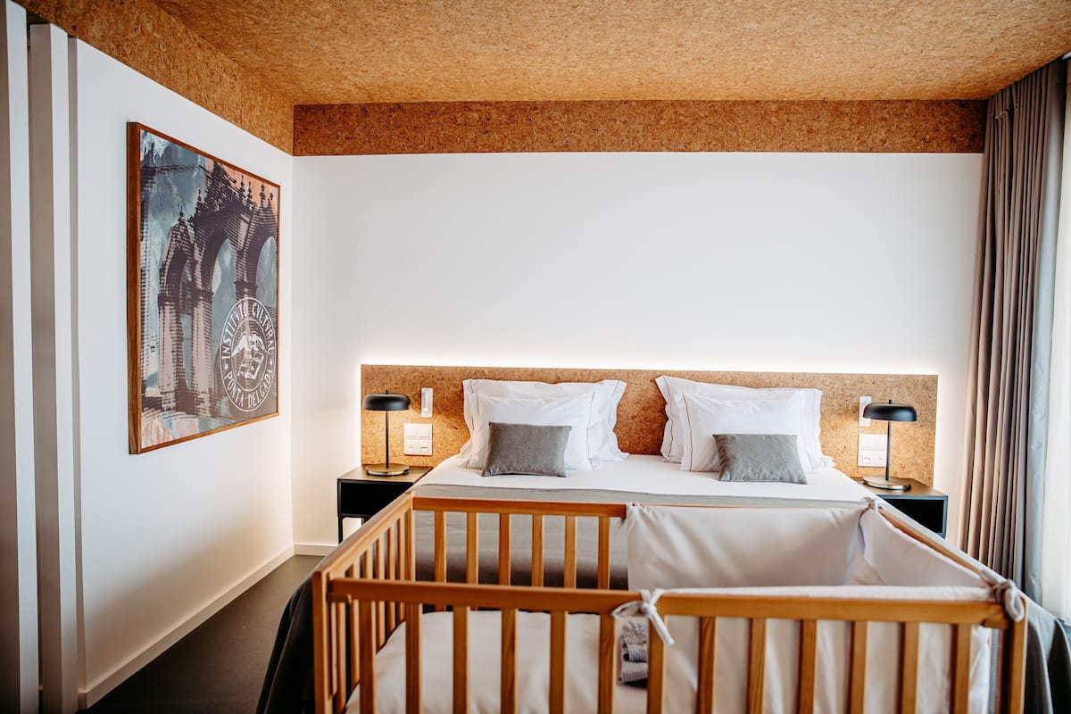 A hotel room with a bunk bed, a wooden crib, a cork ceiling, and a framed picture on the wall.