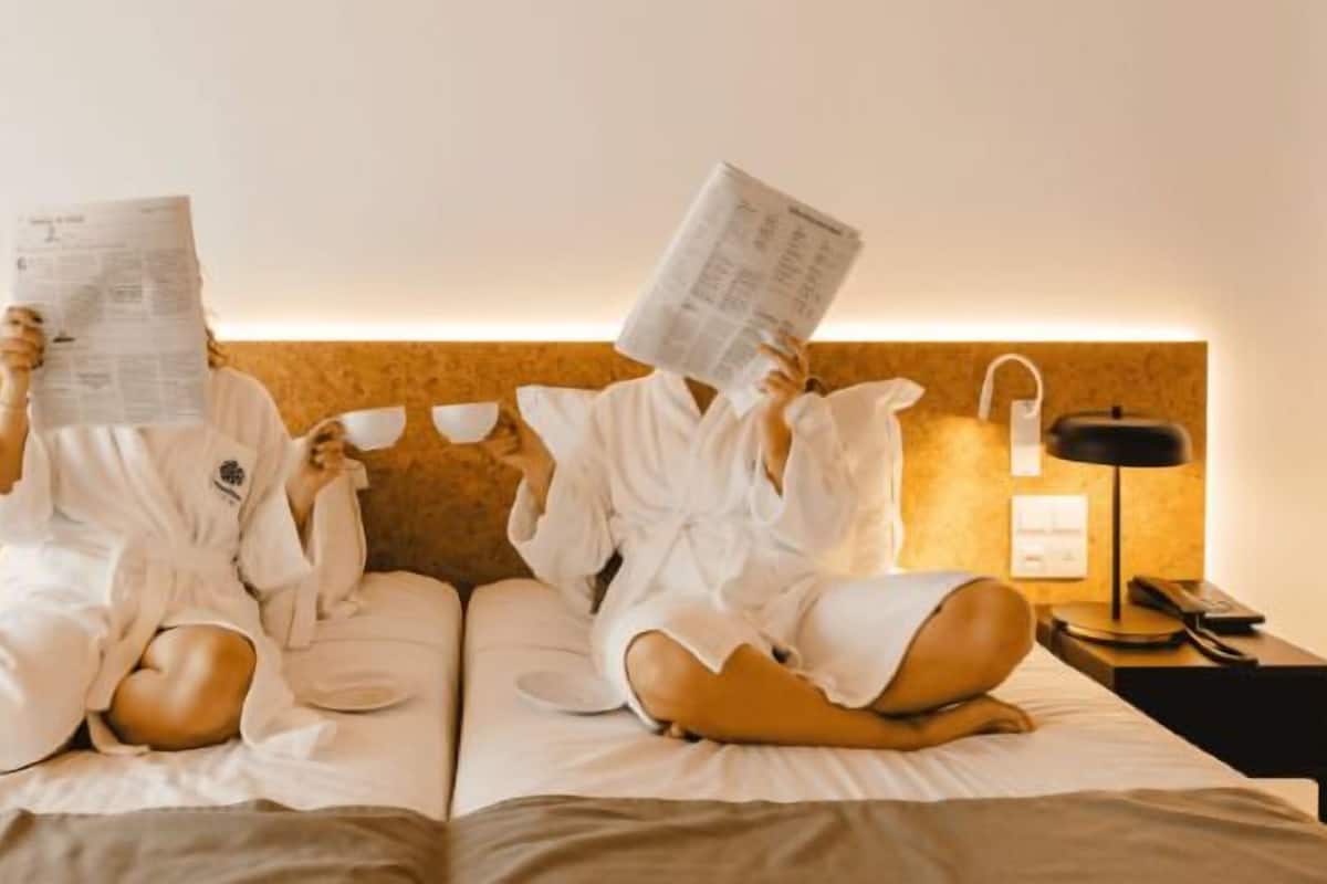 A hotel room with two beds, a wooden headboard, bedside lamps, and a nightstand with a phone.