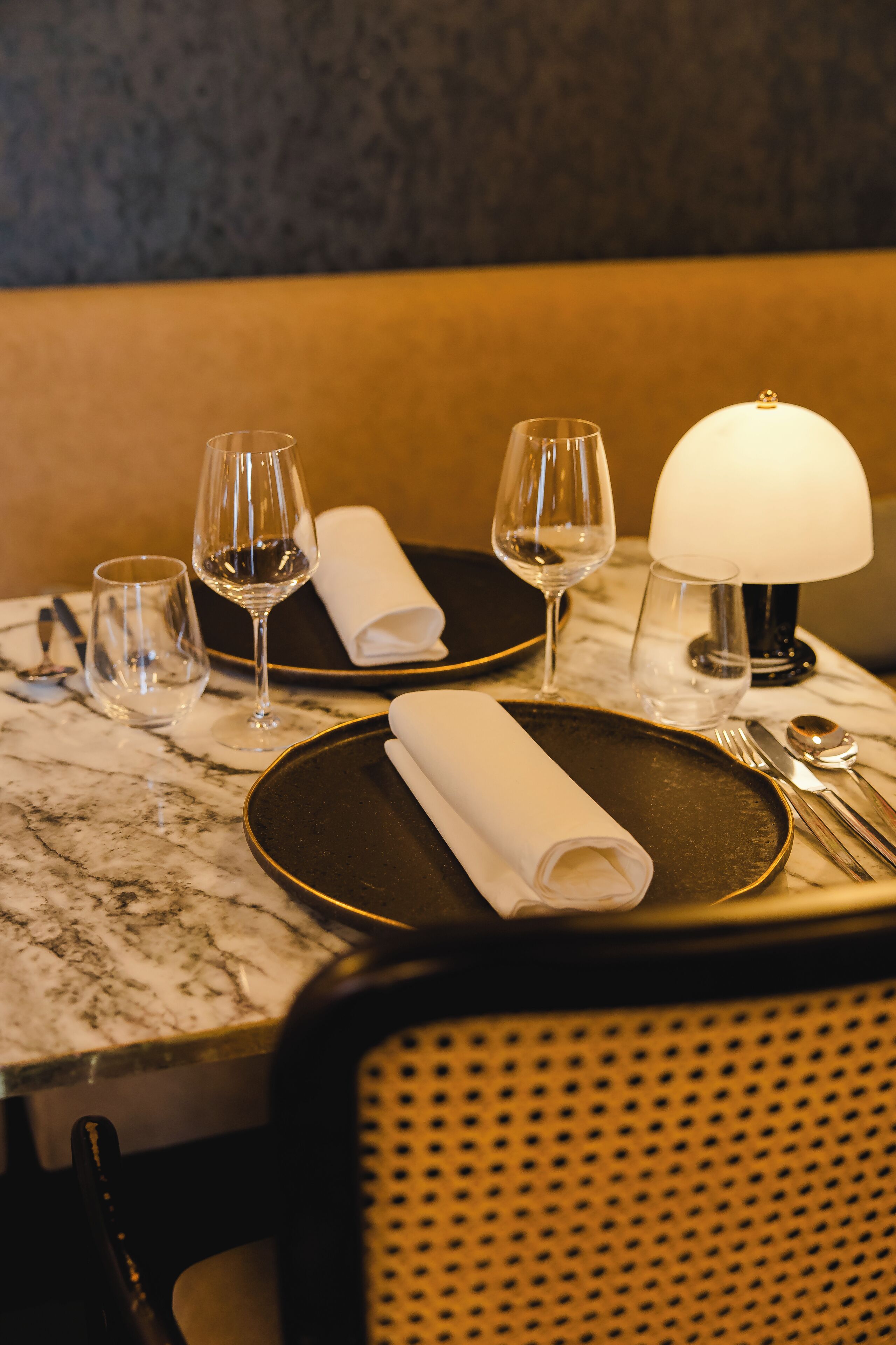 A dining table set with plates, glasses, a folded napkin, cutlery, and a lamp.