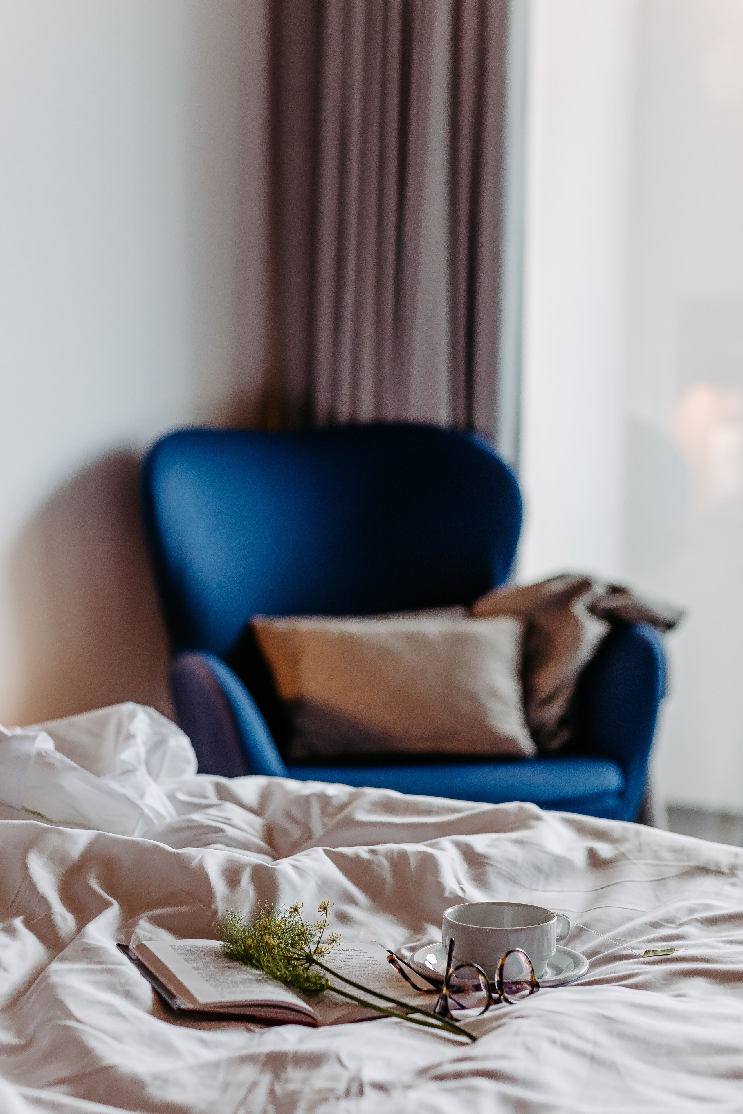 A bed with a book, a pair of glasses, and a cup on a white bedspread.
