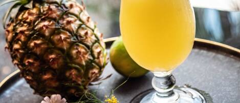 A tropical drink in a glass with a pineapple slice and a flower garnish, a hand holding a straw, and a pineapple on the table.