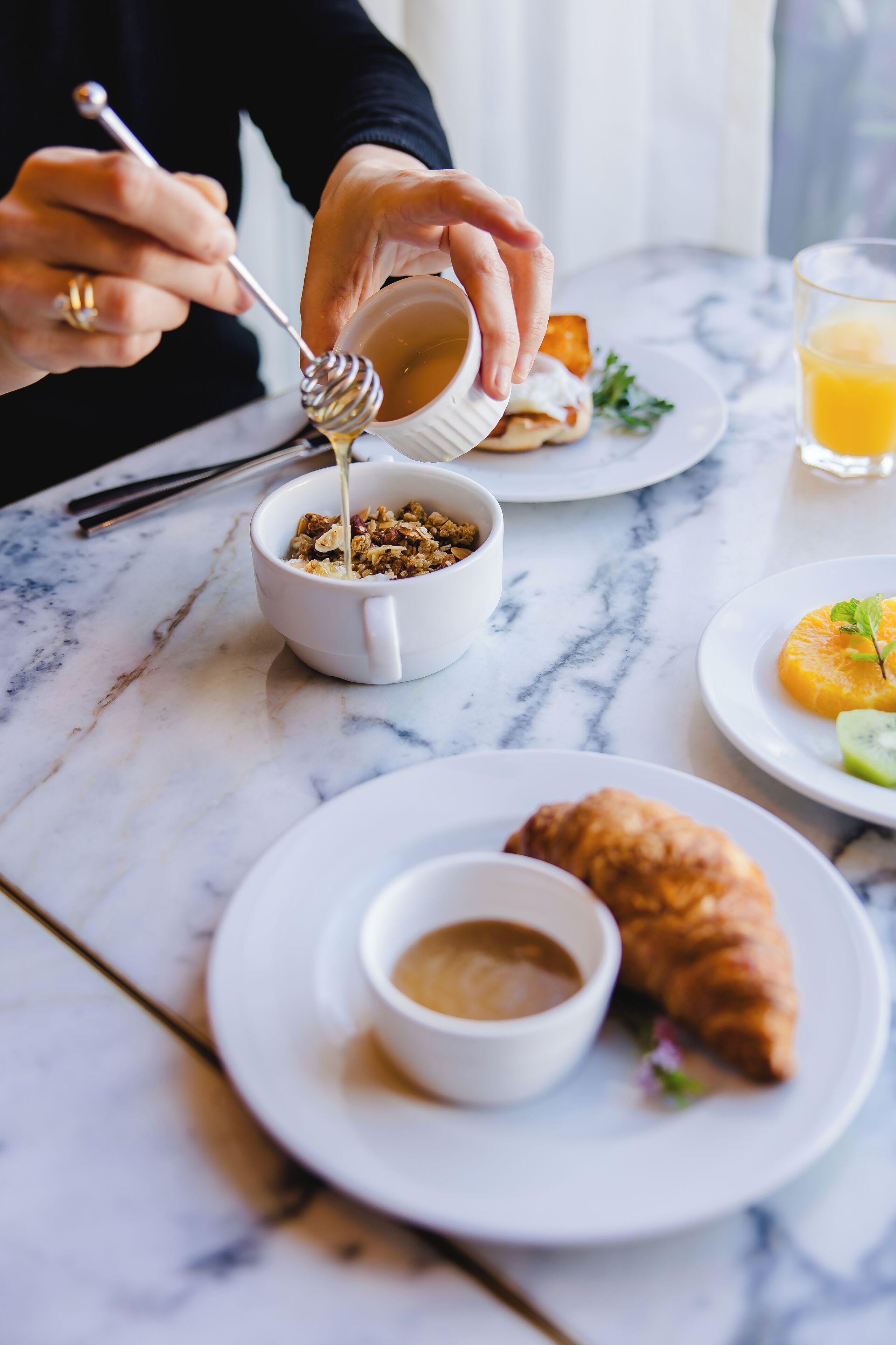 Una mesa de mármol con un croissant, un tazón de granola y un vaso de jugo de naranja.