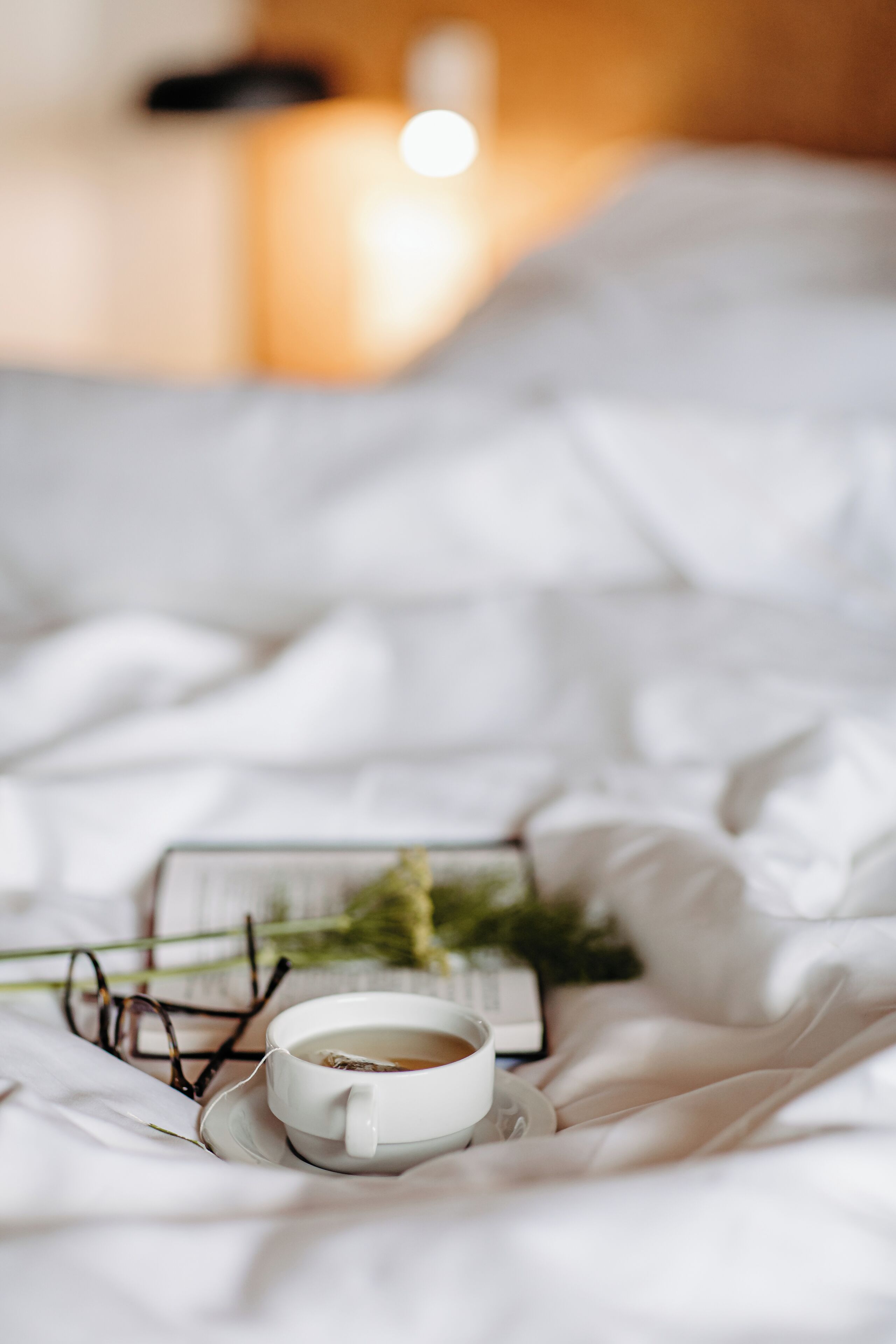 Ein Bett mit einer Tasse Tee, einem Buch und einer Brille auf einer weißen Bettdecke.