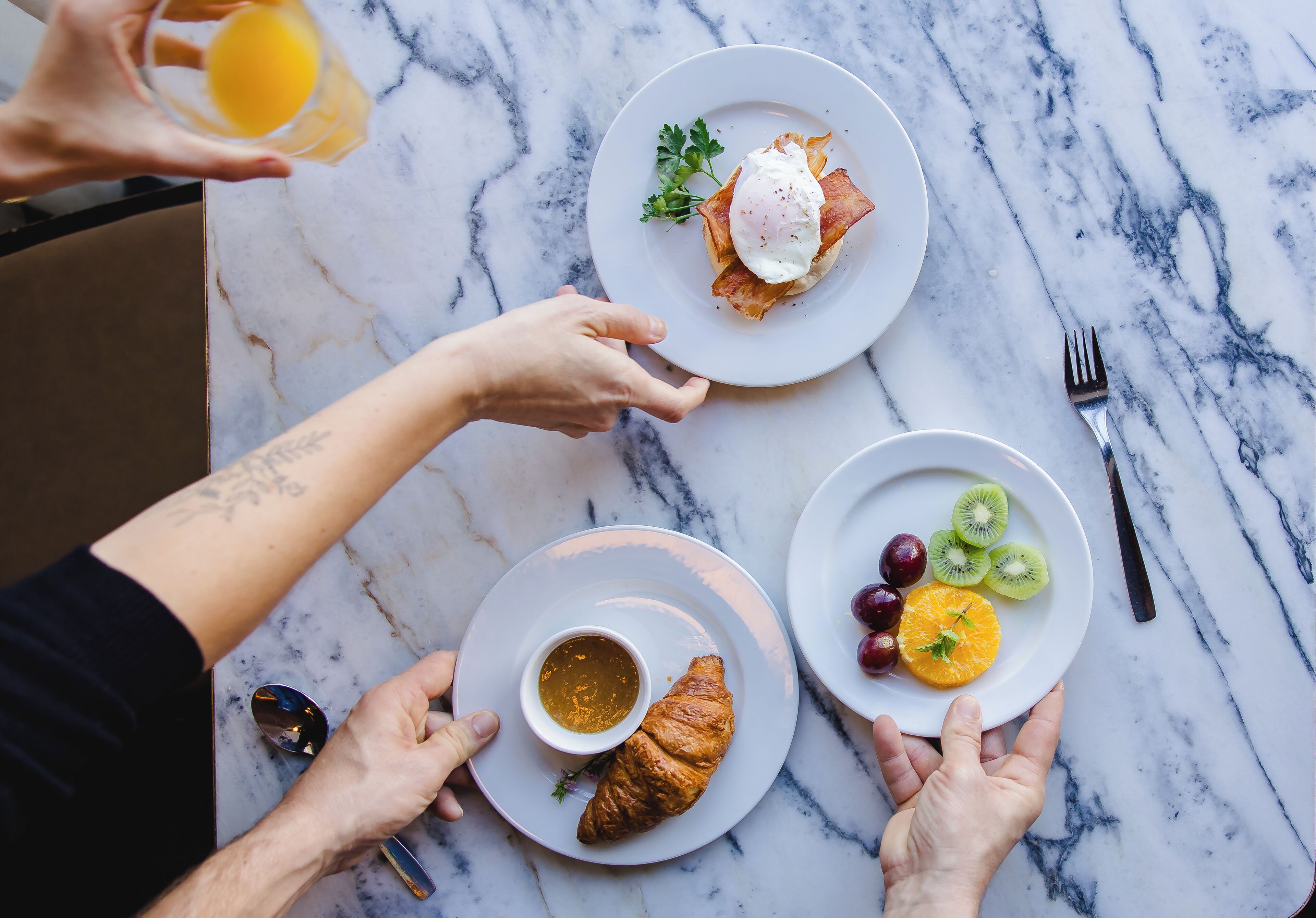 Une table en marbre dressée pour le petit-déjeuner, avec des assiettes remplies de nourriture, notamment des œufs, des croissants et des fruits.