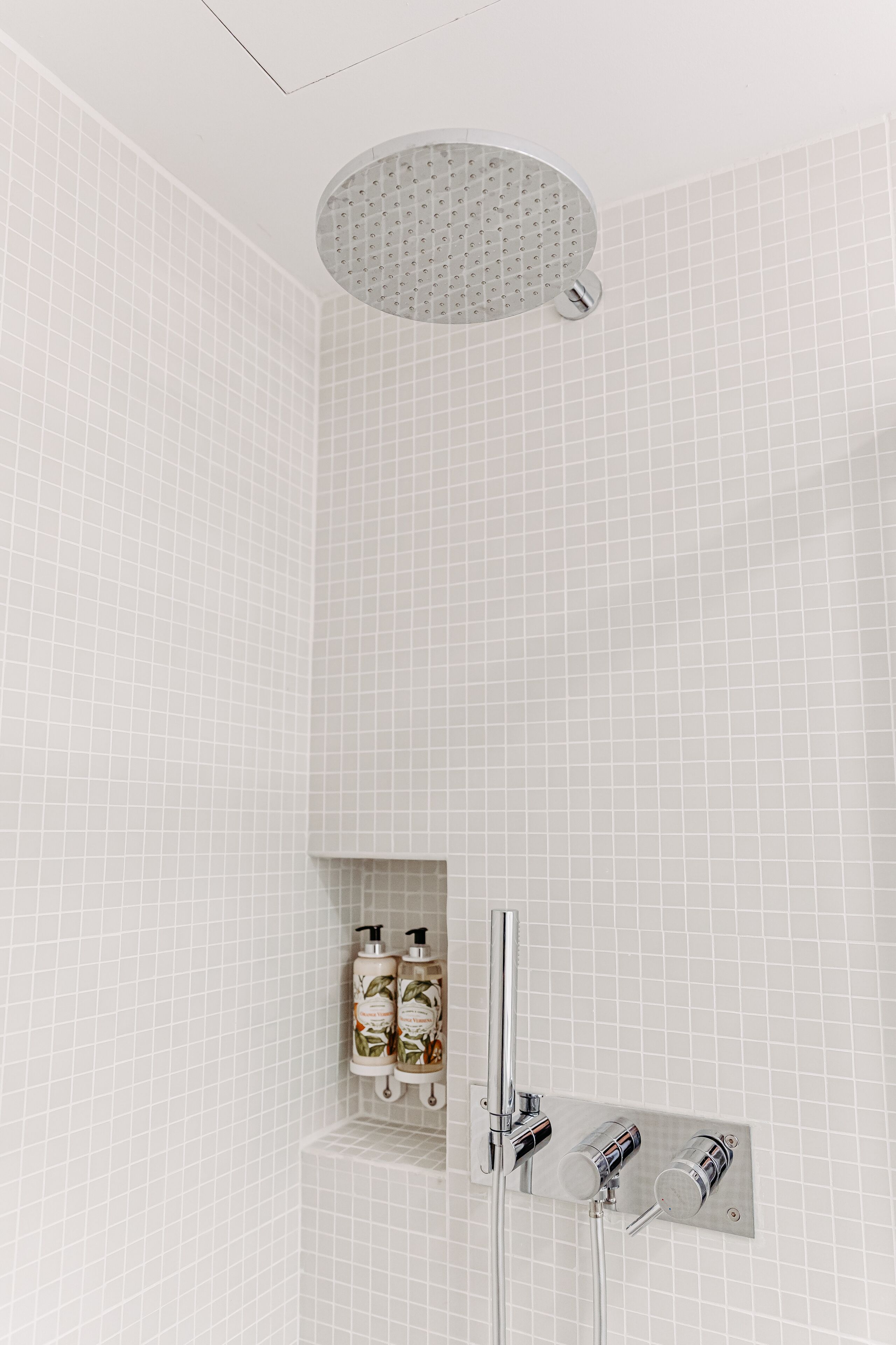 A modern bathroom with a shower, a wall-mounted soap dispenser, and a ceiling-mounted showerhead.