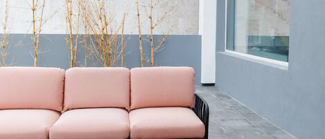 A modern outdoor seating area with a sofa and a small table, a glass of drink, and a book.