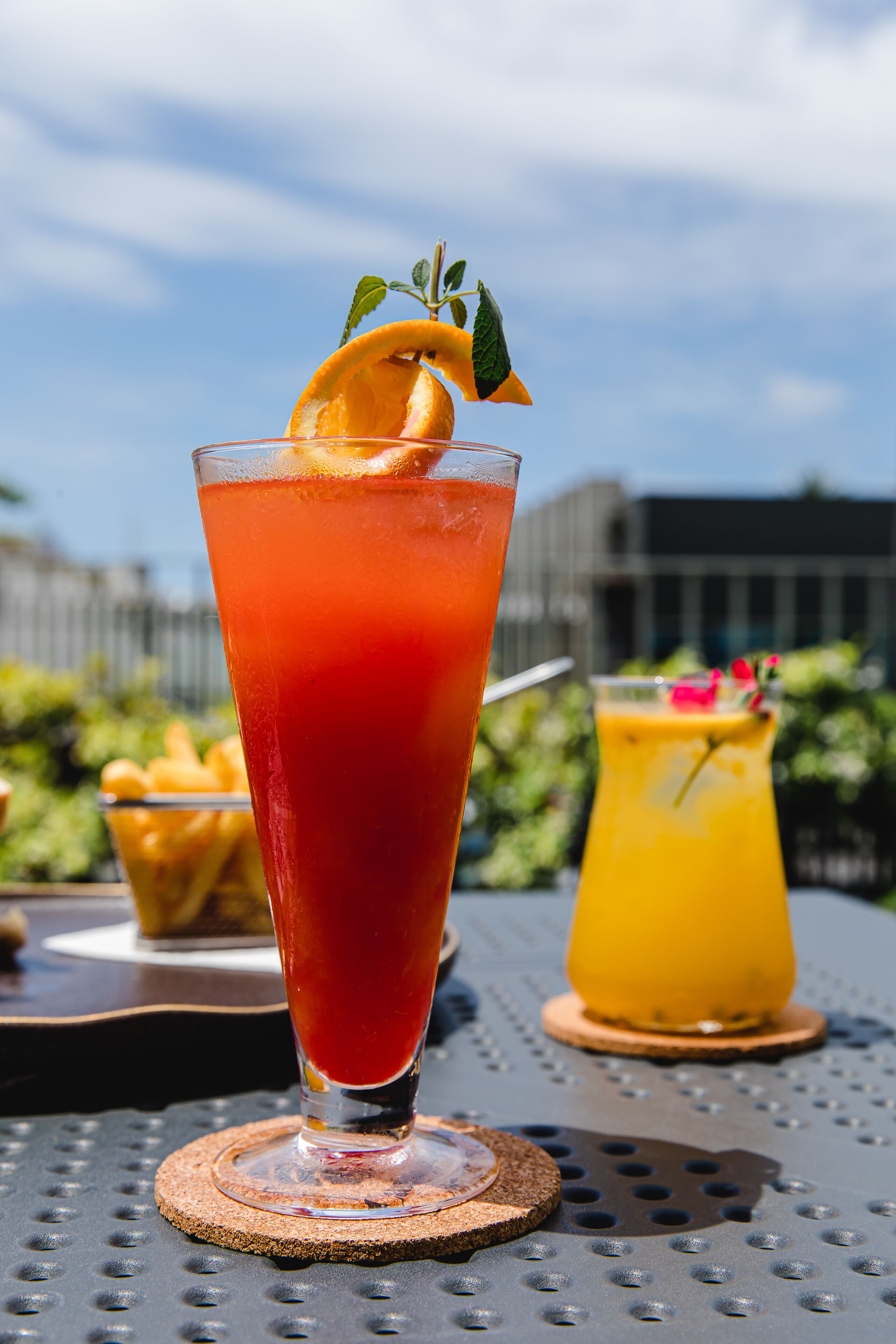 Deux boissons sont posées sur une table dont la surface est en métal : l’une est servie dans un grand verre, l’autre dans un verre plus petit, et les deux sont décorées.
