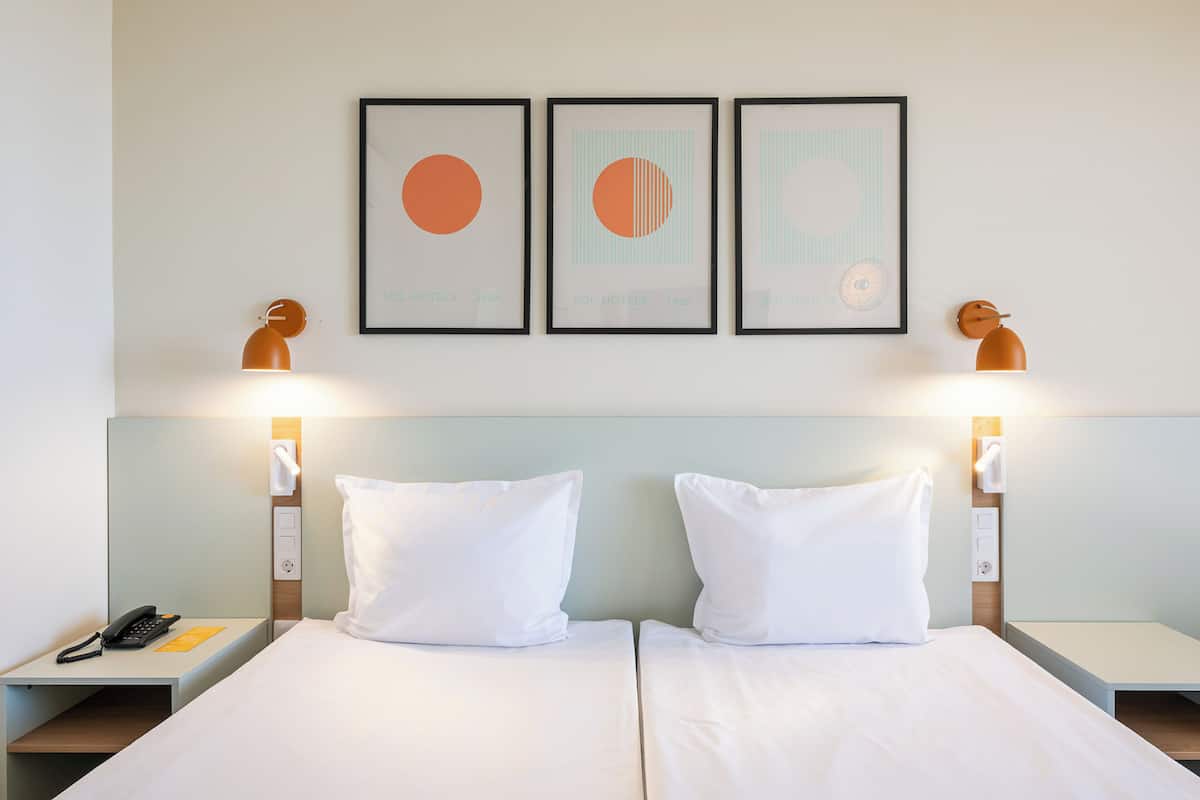 A hotel room with two beds, a phone, and framed artwork on the wall.