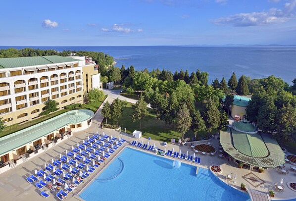 A hotel with a large pool, multiple lounge areas, and a view of the sea.