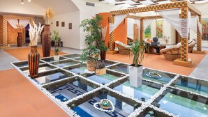 A spacious lobby with a glass floor, decorative vases, potted plants, and a seating area with a cushioned chair and a small table.