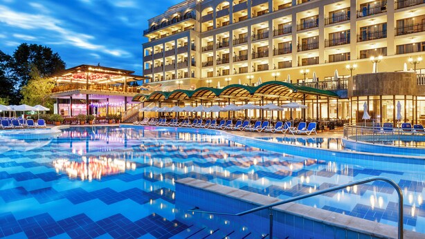 A hotel with a large swimming pool, multiple balconies, and outdoor seating areas.