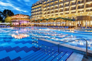 A hotel with a large swimming pool, multiple balconies, and outdoor seating areas.