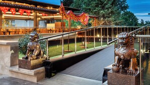 A bridge with two lion statues on either side, leading to a building with outdoor seating and red lanterns.