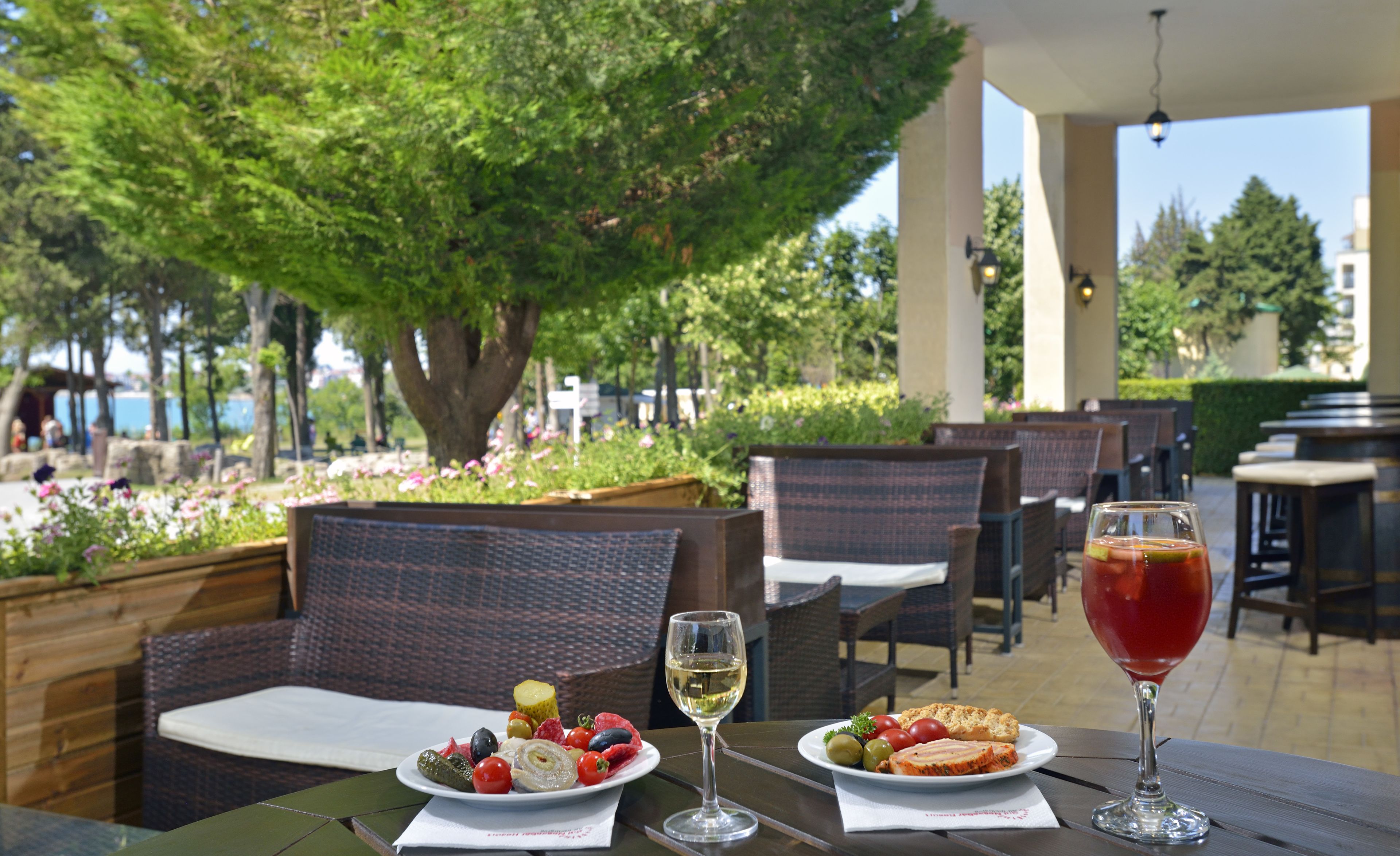 An outdoor dining area with wicker chairs, a table with plates of food, and a glass of red wine.