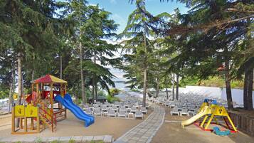 A playground with slides and climbing structures, surrounded by beach chairs and palm trees.