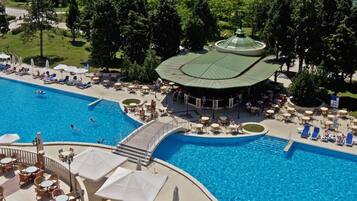 A large outdoor swimming pool with multiple lounge areas and umbrellas, surrounded by trees and a view of the sea.