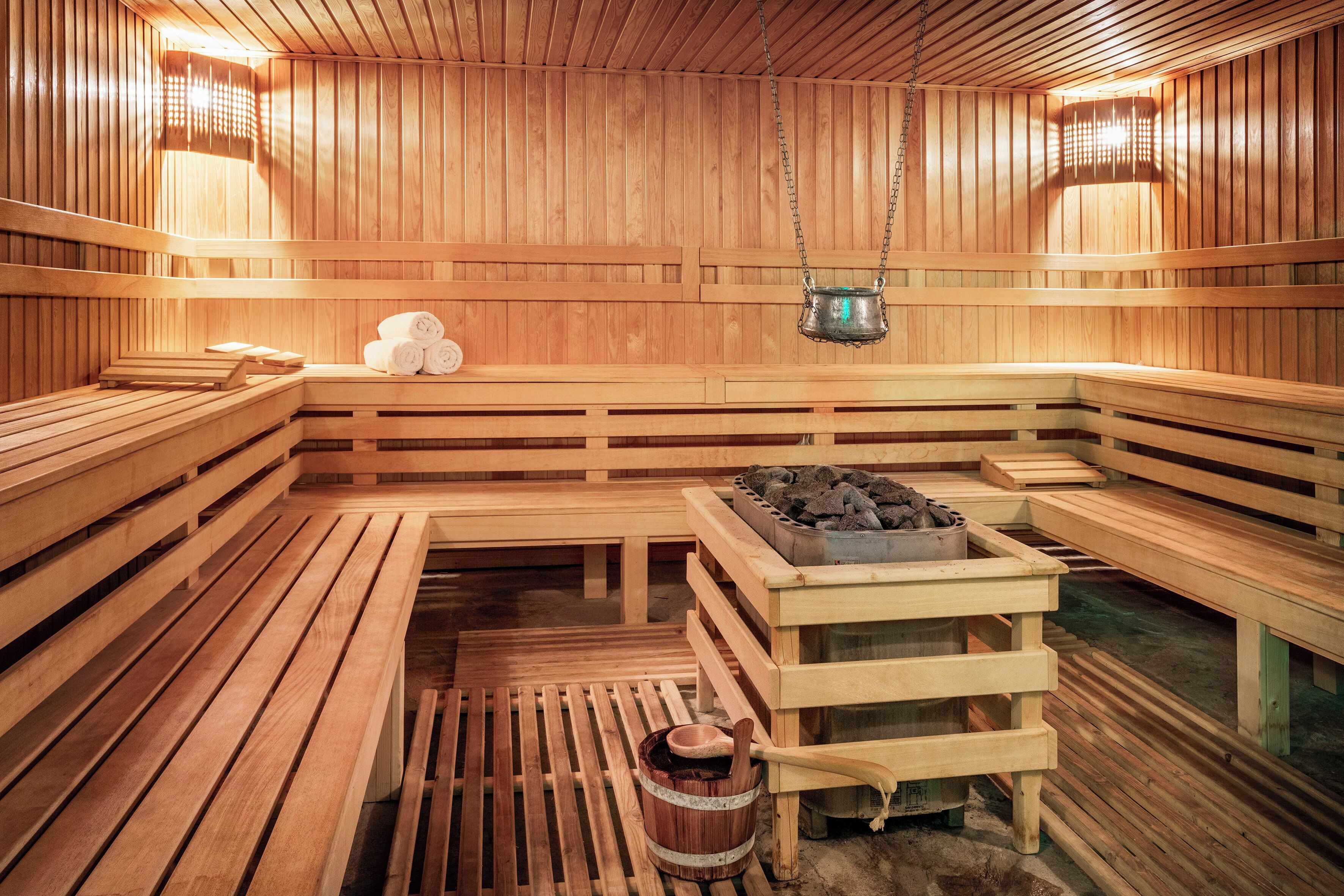 Una sauna de madera con bancos, una mesa de calefacción central y una lámpara colgante.