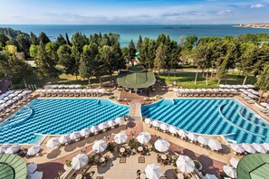 Un resort con dos piscinas grandes, zonas de estar al aire libre y vista al mar.
