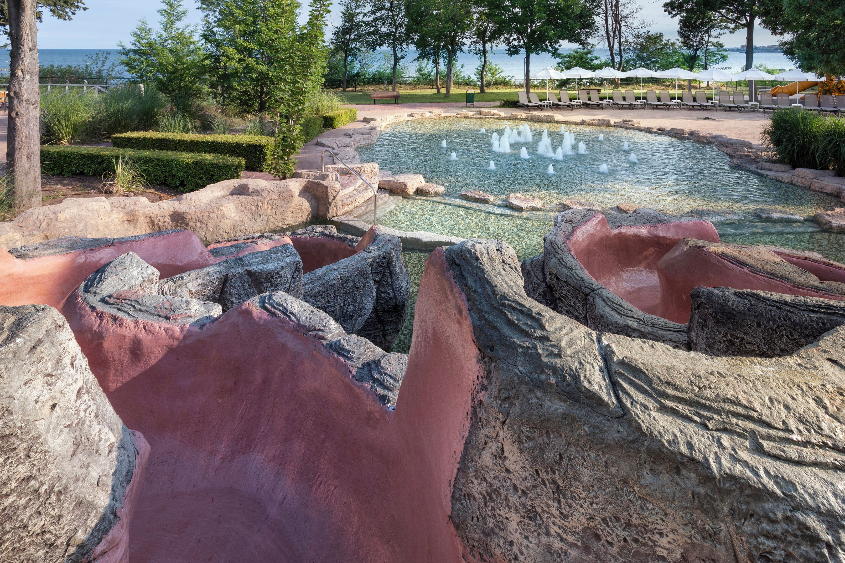 A landscaped area with a pool, seating, and a view of the water.