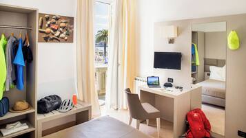 A hotel room with a bed, a desk with a laptop, a TV, a mirror, a wardrobe, and a window with curtains.