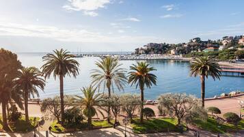Un paisaje urbano costero con un puerto deportivo, palmeras y un paseo marítimo.