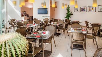 A restaurant with wicker furniture, hanging pendant lights, and framed artwork on the walls.