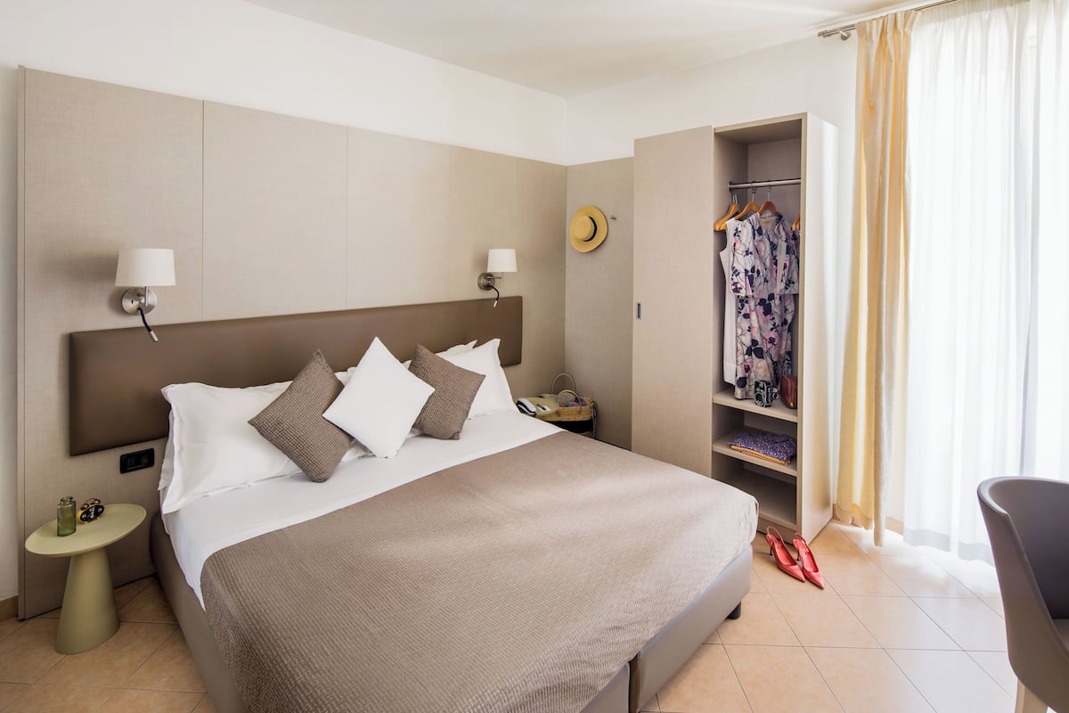 A hotel room with a large bed, bedside lamps, a wardrobe, and a chair.