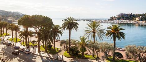 A coastal road with palm trees, a marina, and a bridge in the background.