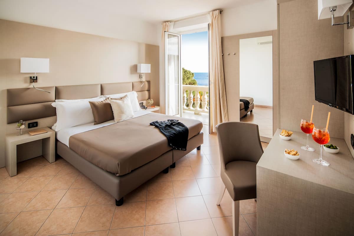 A hotel room with a bed, bedside tables, a desk with a chair, a TV, and a balcony with a view.