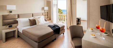 Habitación de hotel con cama, mesitas de noche, escritorio con silla, televisor y balcón con vistas.
