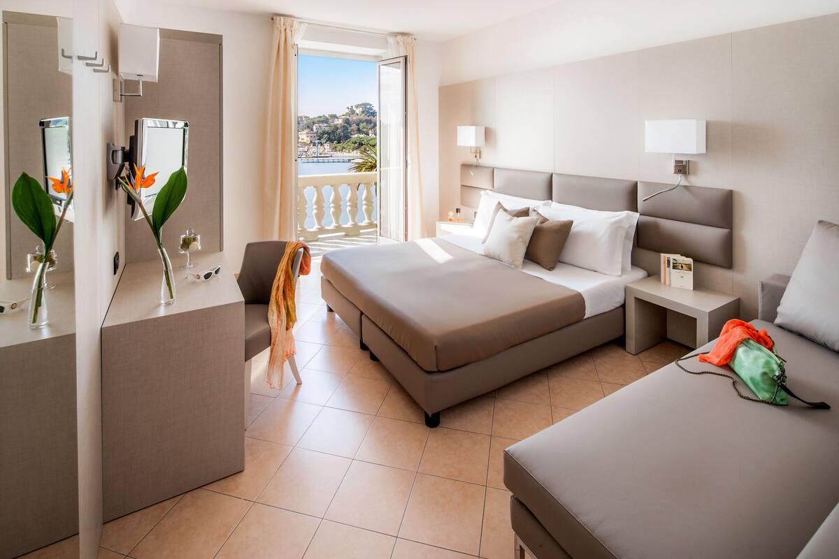 A hotel room with a bed, a desk, a chair, a balcony with a view, and a bathroom.