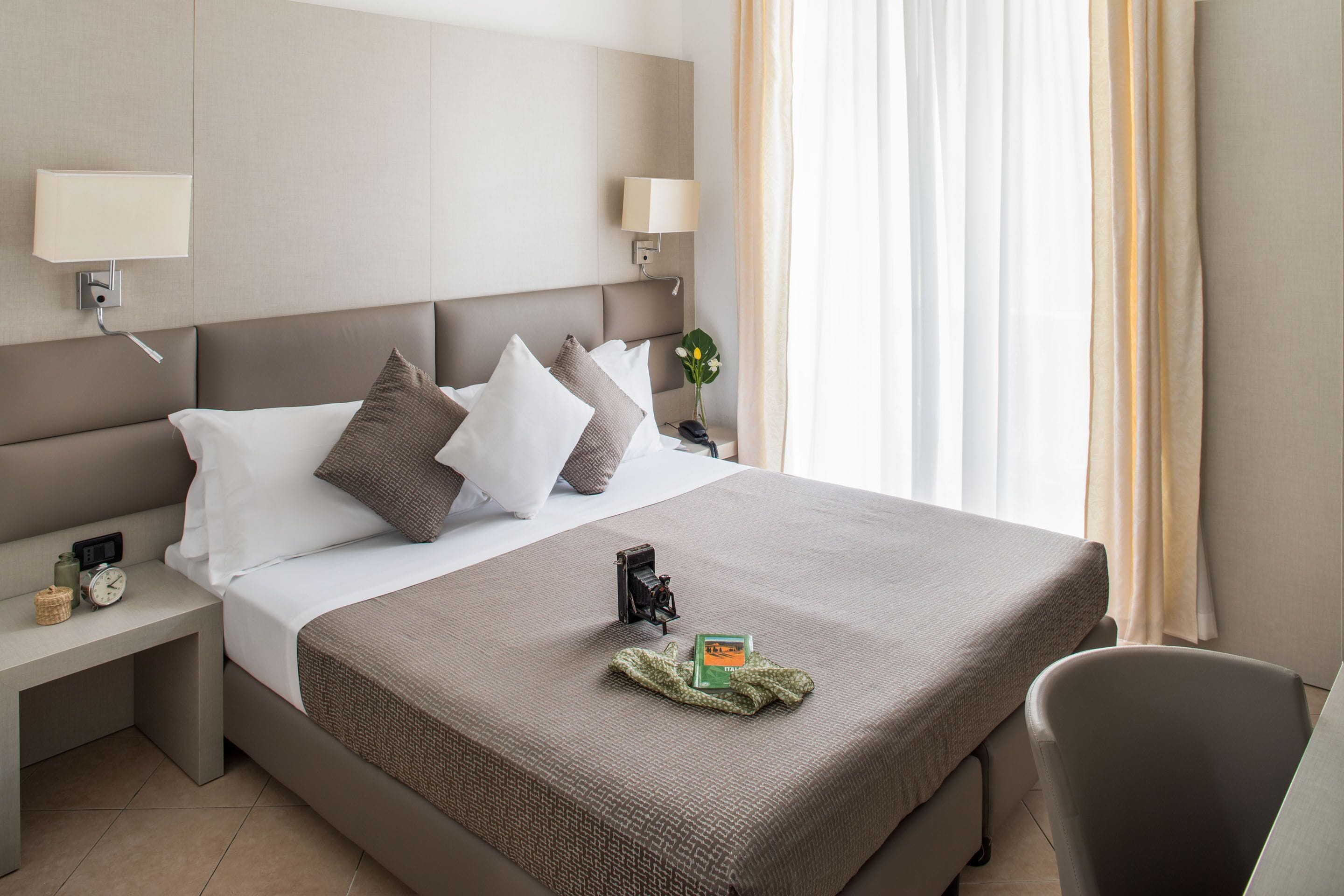 Un letto rifatto con una coperta marrone, un comodino con una lampada e una sedia.