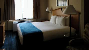 Une chambre d’hôtel avec un grand lit, une table de chevet, une lampe, une chaise et une fenêtre avec des rideaux.