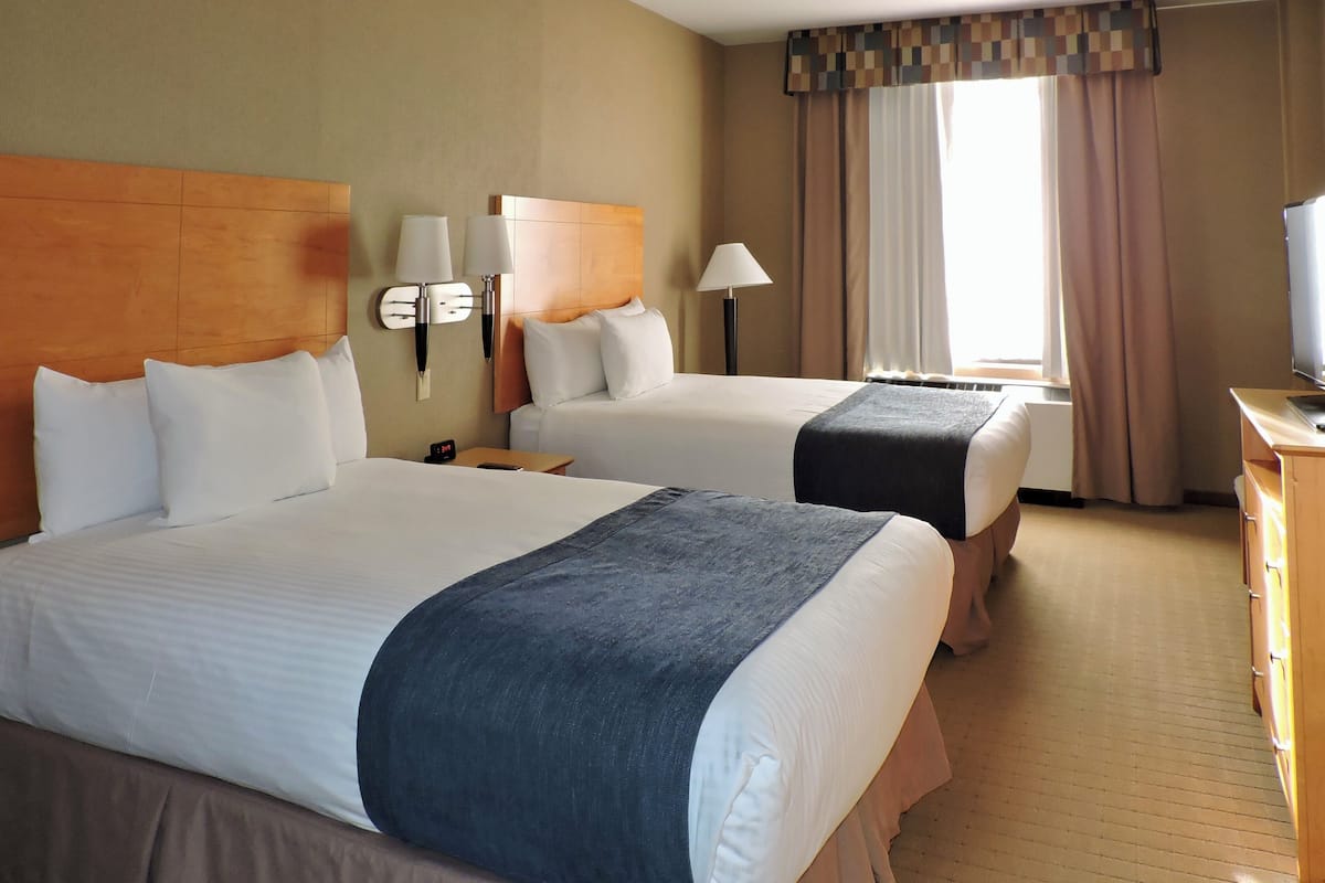 A hotel room with two beds, a television, a desk, and a window with curtains.