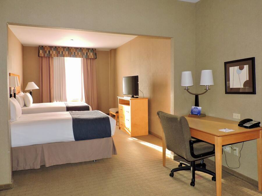 A hotel room with two beds, a desk, a chair, a television, and a telephone.
