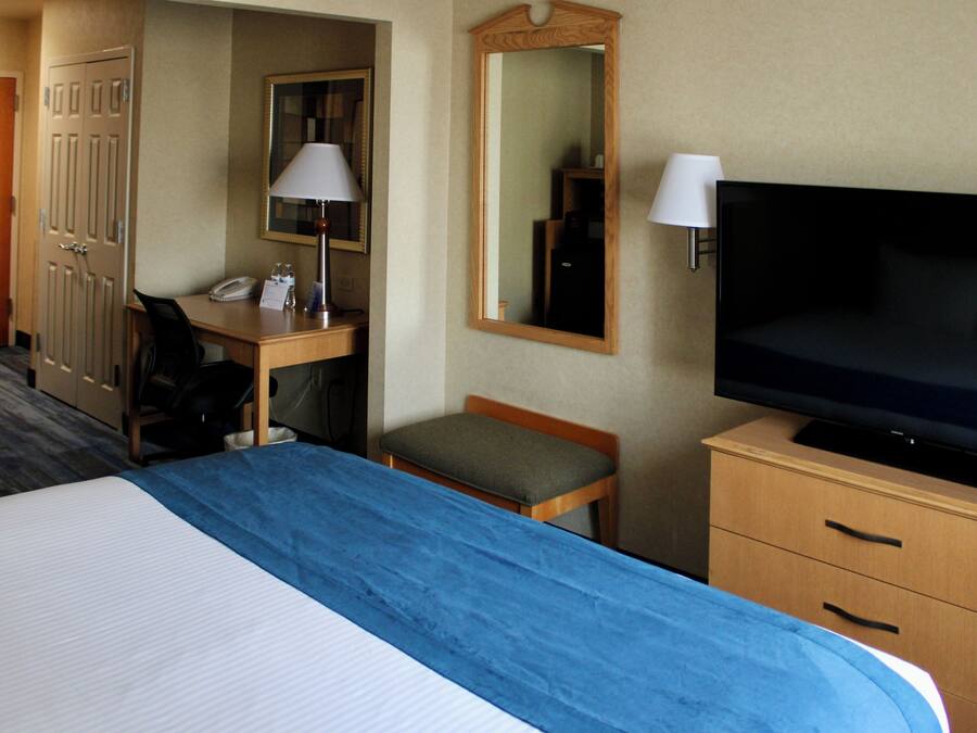 Ein Hotelzimmer mit einem Bett, einem Schreibtisch mit Telefon, einem Sessel, einem Fernseher und einem Spiegel.