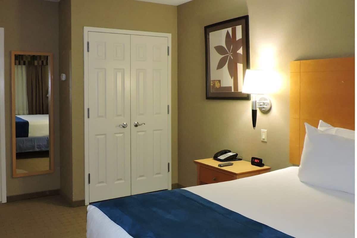 A hotel room with a large bed, a bedside table with a lamp, a clock, and a mirror.