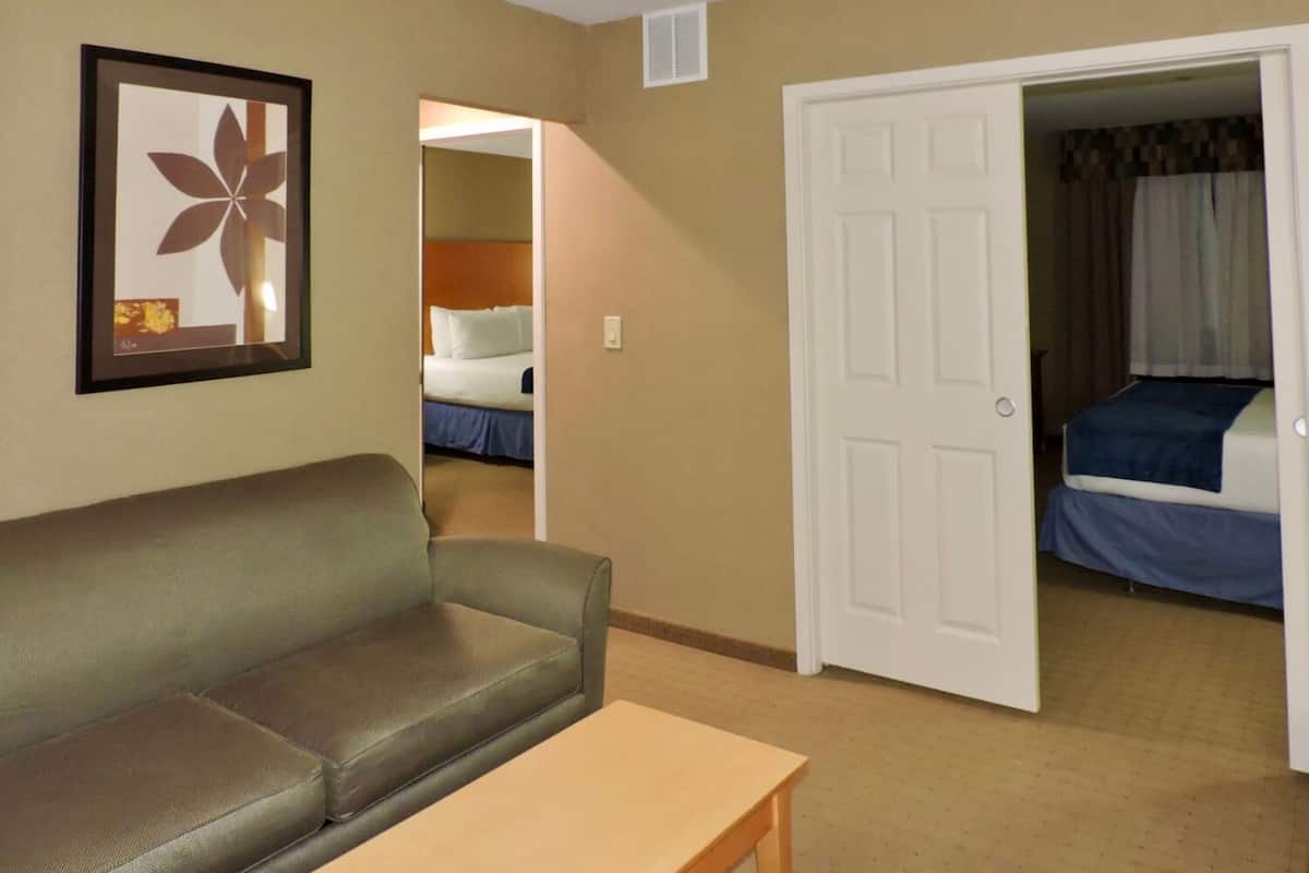 A hotel room with a sofa, a table, a door leading to another room, and a framed picture on the wall.