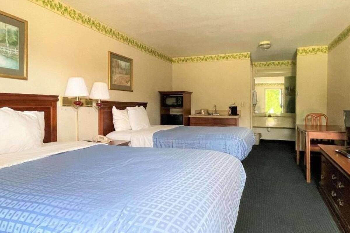 A hotel room with two beds, a desk, a chair, a television, and a mirror.