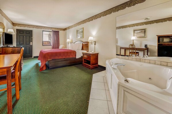 A hotel room with a bed, a desk with a chair, a desk lamp, a telephone, a mirror, a television, and a bathtub. - Rodeway Inn Sandersville (Sandersville)