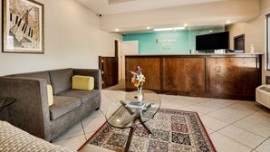 A lobby with a reception desk, a flat-screen TV, a sofa, and a coffee table with a vase of flowers.