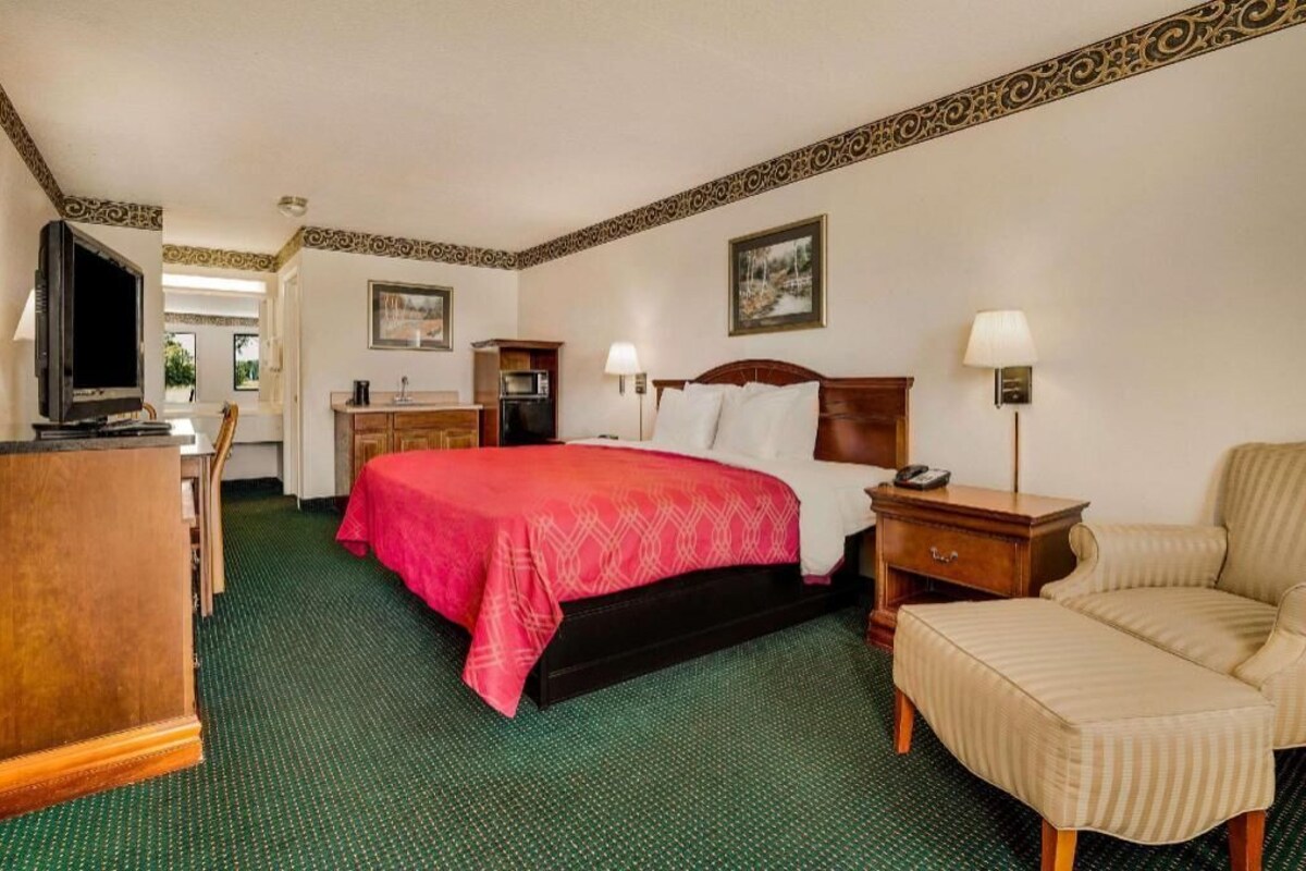 A hotel room with a bed, a TV, a desk, a chair, and a lamp.