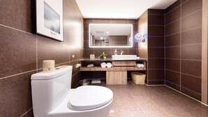 Une salle de bain moderne avec des toilettes blanches, un meuble-lavabo en bois, un grand miroir et des murs recouverts de carreaux de couleur marron foncé.
