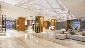 Un hall d’hôtel moderne avec un sol en marbre, un comptoir d’accueil et un espace détente avec des canapés.