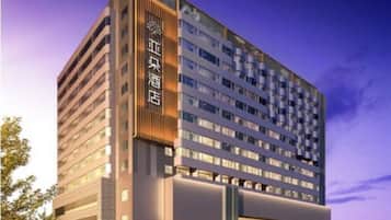 Un hôtel moderne à plusieurs étages, doté d’une entrée imposante et d’un parking pouvant accueillir plusieurs voitures.
