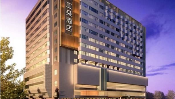 Un hôtel moderne à plusieurs étages, doté d’une entrée imposante et d’un parking pouvant accueillir plusieurs voitures.