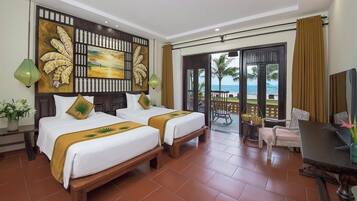 Habitación de hotel con dos camas, un balcón con vistas a la playa y un comedor con mesa y sillas.