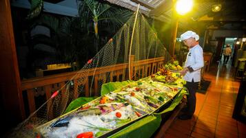 A seafood display with a variety of fish and seafood, a chef standing beside it, and a tropical background with a thatched roof.