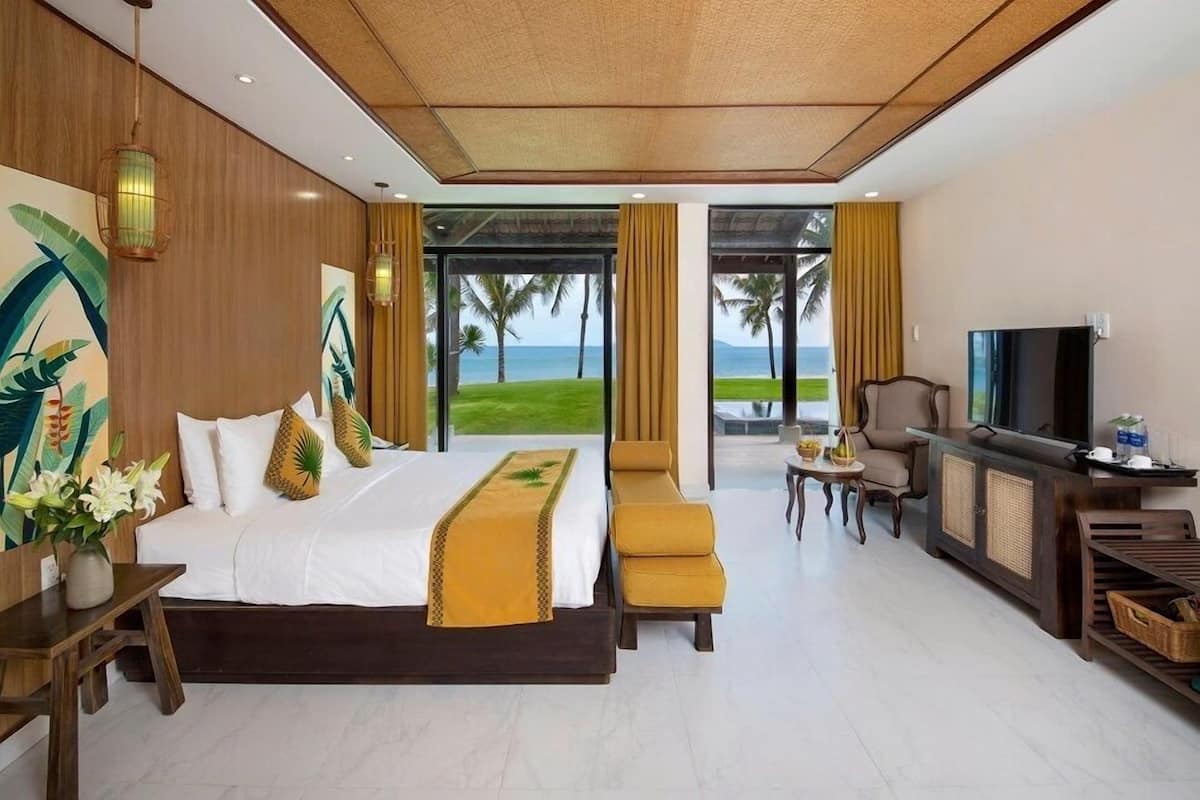 A hotel room with a large bed, a TV, a desk, and a view of the ocean.